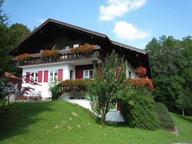 A charming house with a balcony and flower arrangements. Surrounded by green landscape and trees.