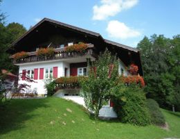 A charming house with a balcony and flower arrangements. Surrounded by green landscape and trees.