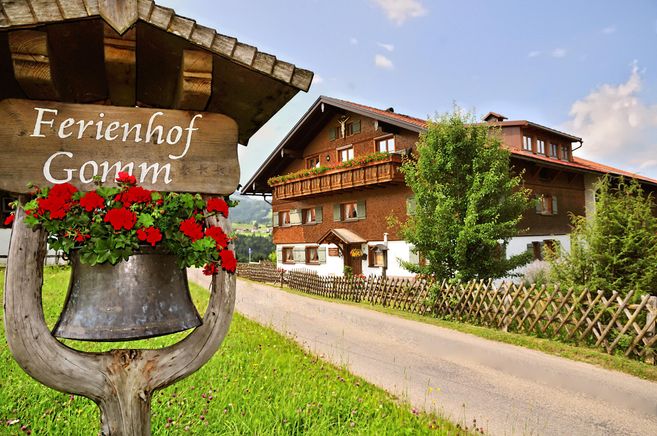 A cozy holiday farm with attractive wooden architecture and colorful flowers. The surroundings are green and inviting, perfect for a relaxing stay.