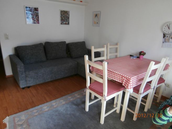 A simple living room with a gray sofa and a dining table with a checkered tablecloth. The decor is straightforward and cozy.