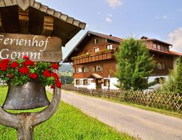 A cozy holiday farm with attractive wooden architecture and colorful flowers. The surroundings are green and inviting, perfect for a relaxing stay.